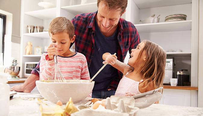 Foto de pai com dois filhos, um menino e uma menina na cozinha preparando alimentos