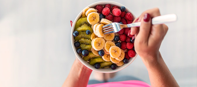 imagem de um recipiente com frutas e uma mão feminina segurando um garfo