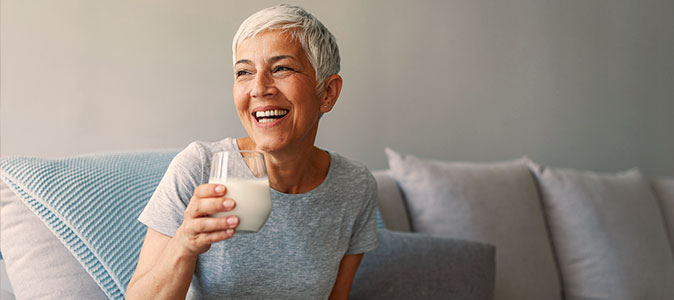 Imagem de uma mulher sorrindo com um copo de leite na mão