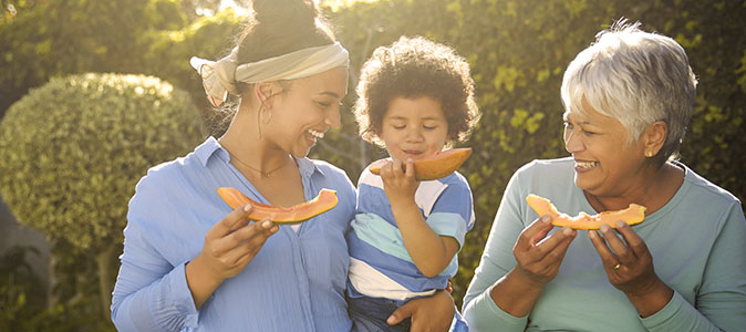 imagem de uma mulher idosa, adulta e bebe comendo mamão