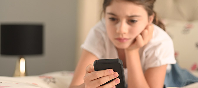 Jovem deitada na cama, usando um celular