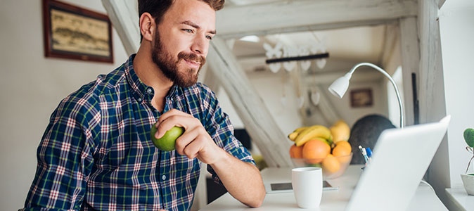 rapaz trabalhando em casa e comendo uma fruta